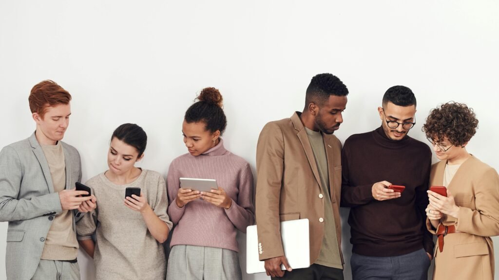 Five adults in casual wear using phones and tablets indoors, emphasising technolog. This is used for Abuse and Rights Policy